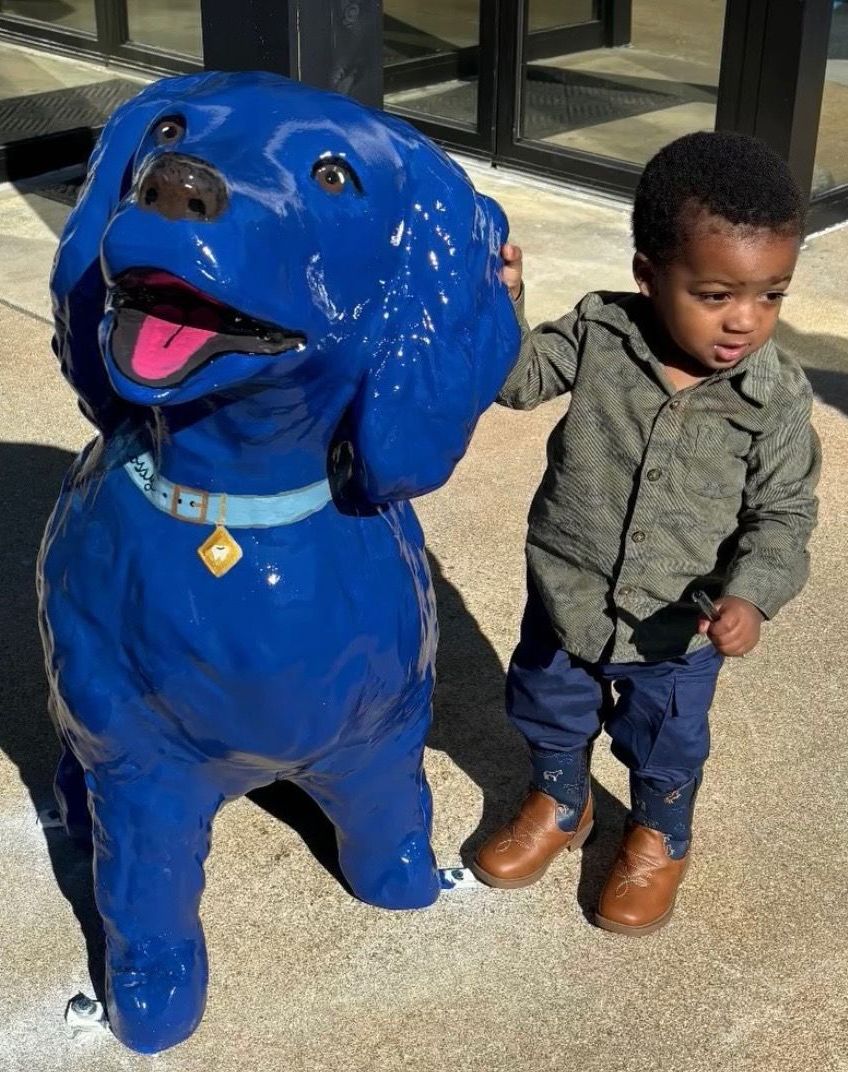 Child stands next to a large blue dog statue; both look to the side.