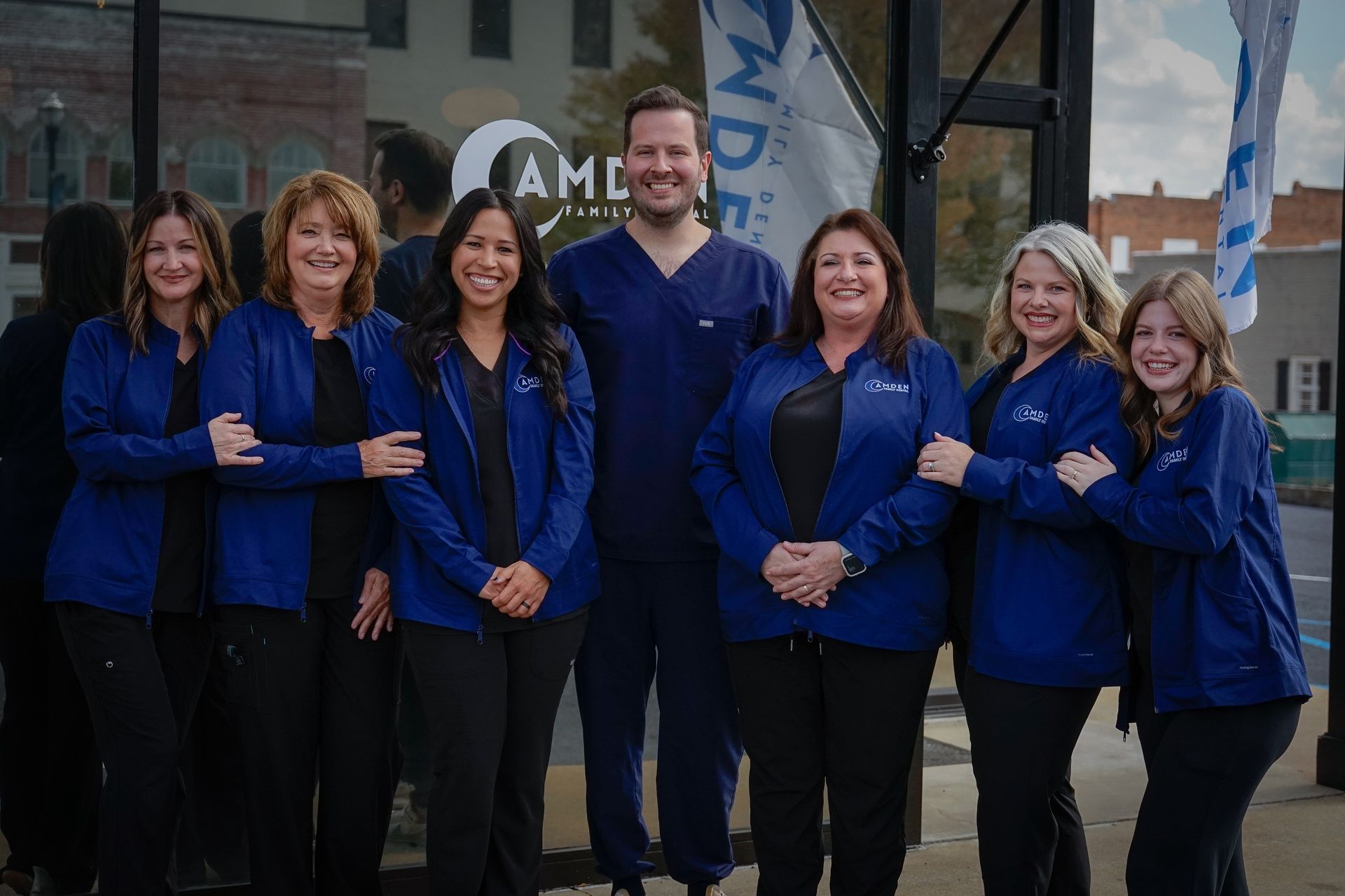 Medical staff in navy scrubs and jackets posing outside a clinic.