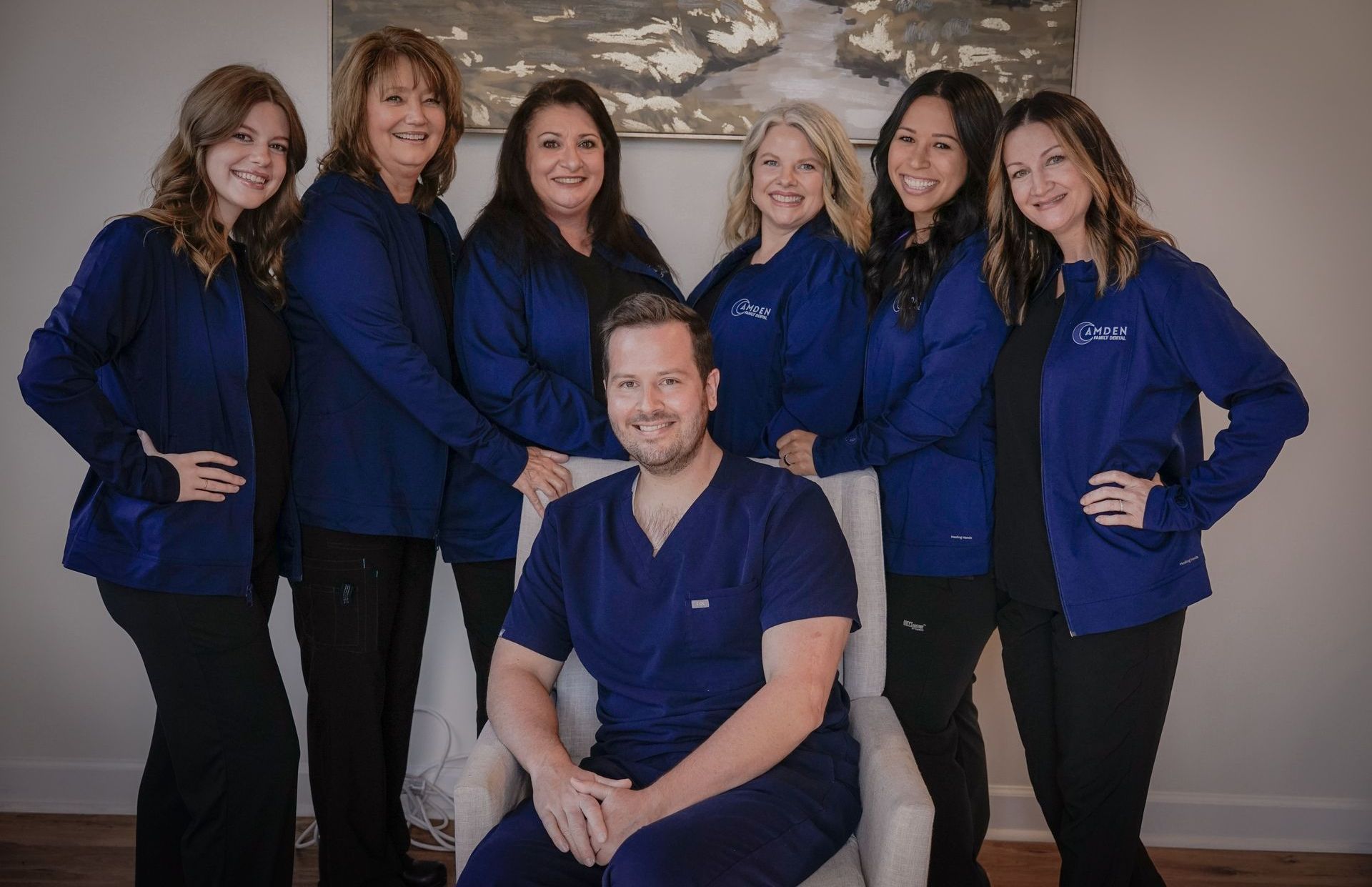 Group of medical professionals in blue scrubs, smiling and posing in a well-lit office.