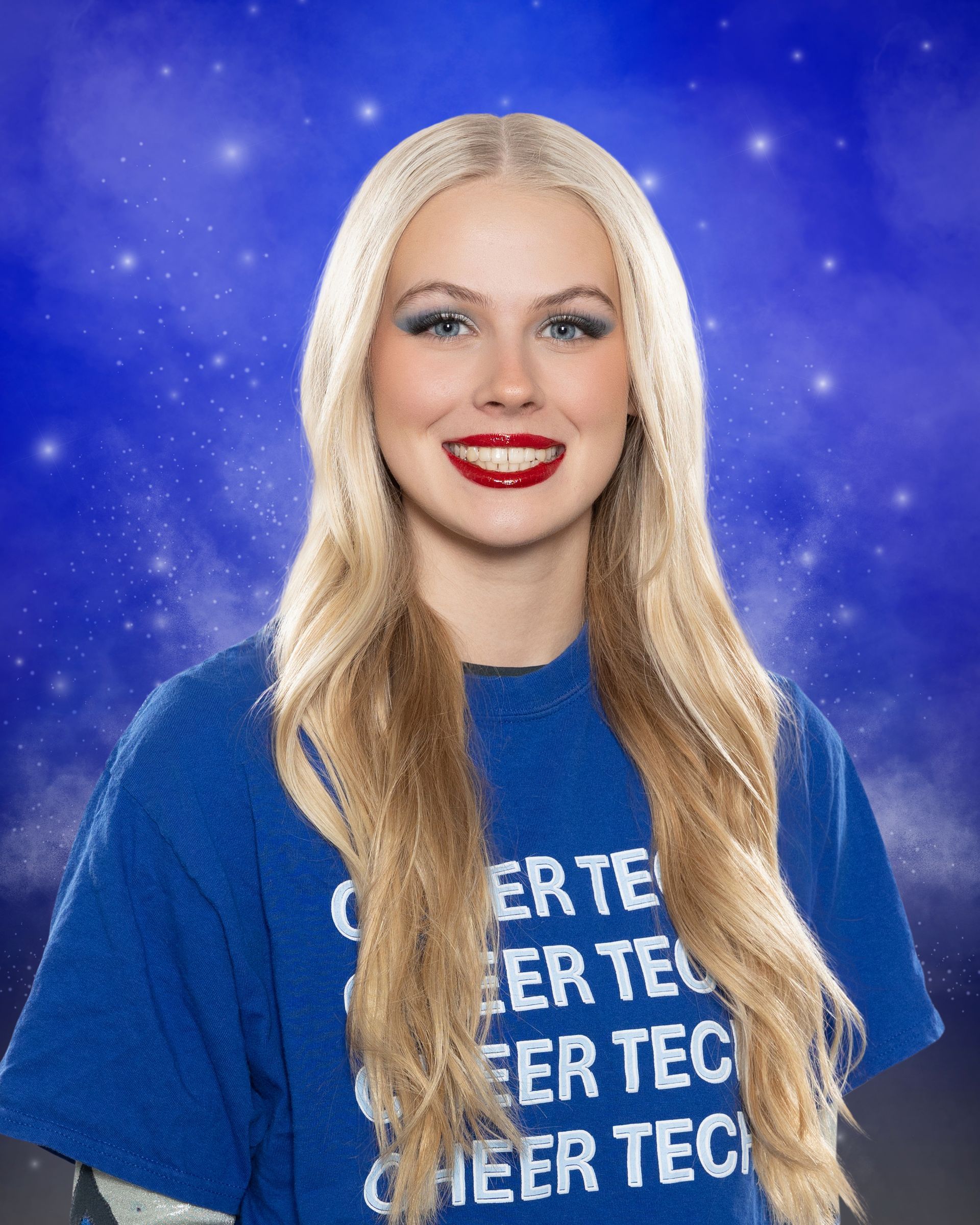 A blonde woman wearing a blue shirt that says cheer tec is smiling.