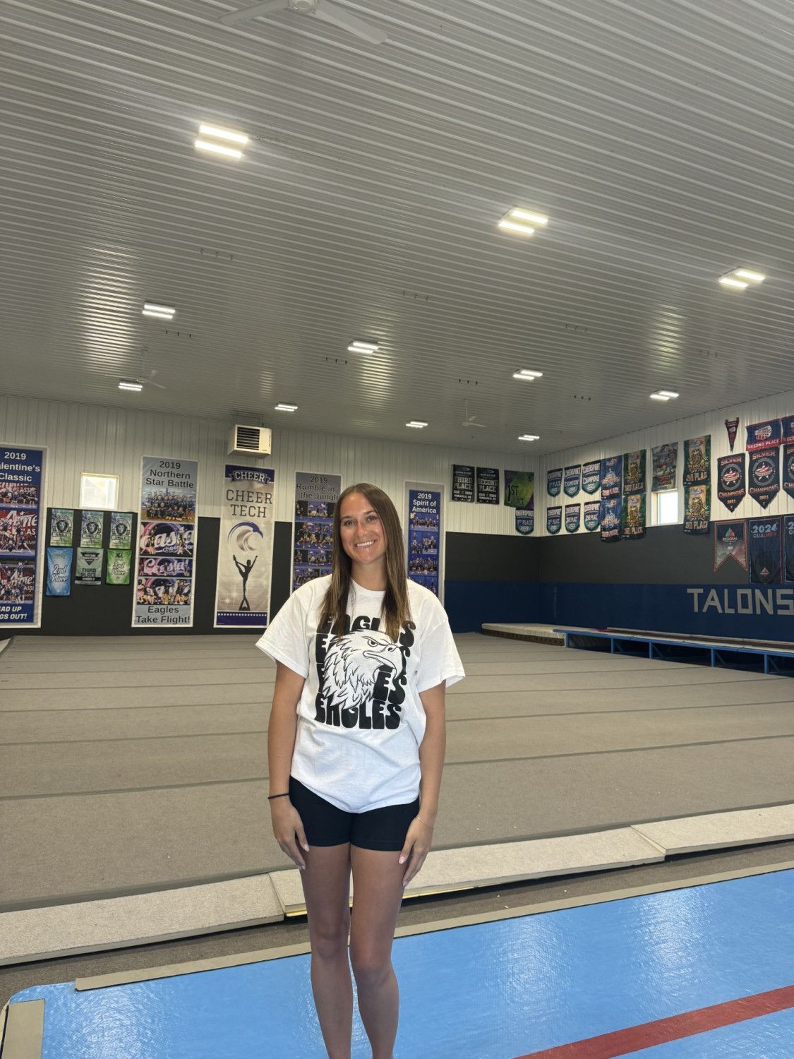 A woman in a white shirt is standing in a gym.