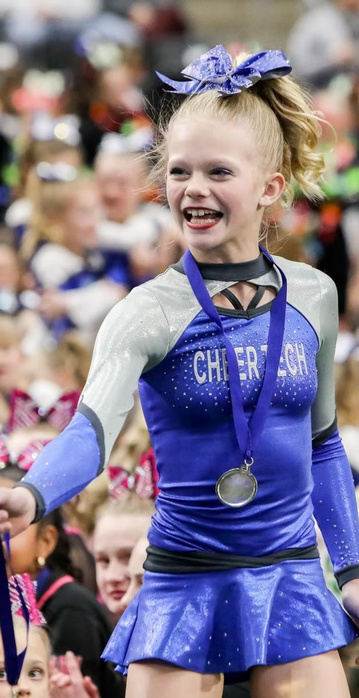 A young girl in a cheerleading uniform is wearing a medal.
