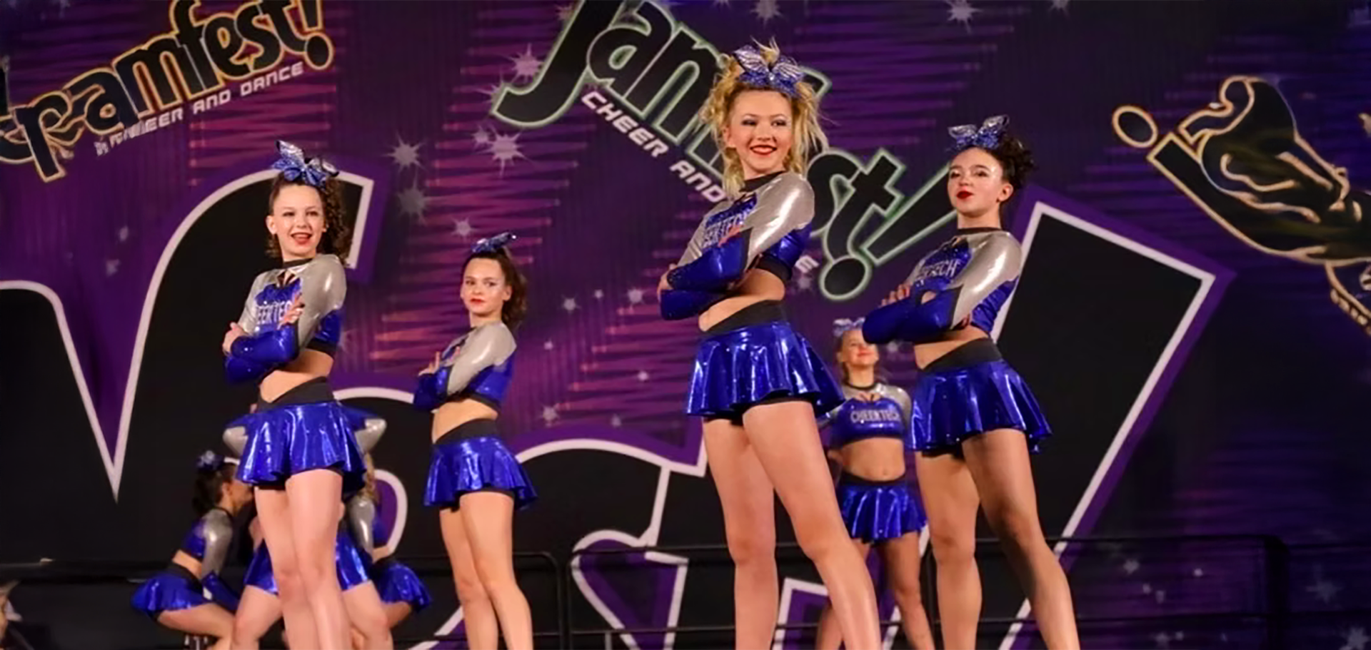 A group of cheerleaders are standing in front of a purple background.