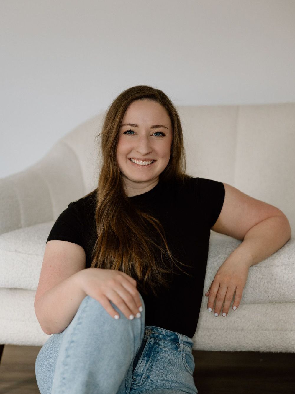 A woman is sitting on a couch with her legs crossed and smiling.