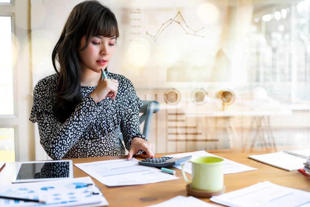 A Woman Is Sitting at A Table Using a Calculator and A Pen — Adding Value CFO Pty Ltd in Darwin, NT
