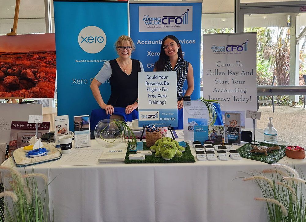 Two Women Standing Behind a Table Offering Free Training— Adding Value CFO Pty Ltd in Larrakeyah, NT