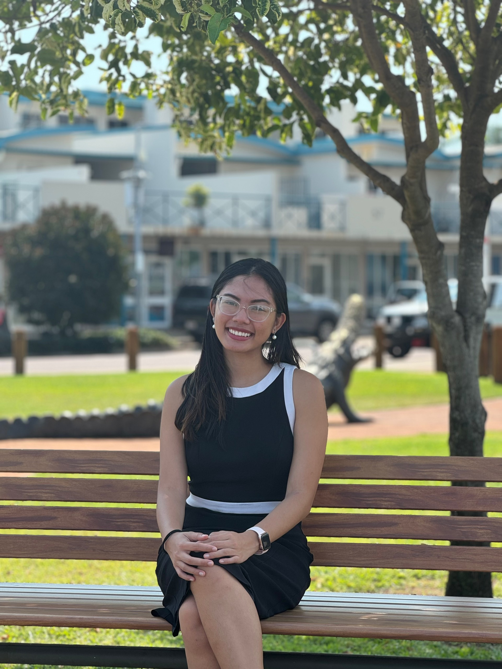 A woman in a black dress is sitting on a wooden bench in a park.