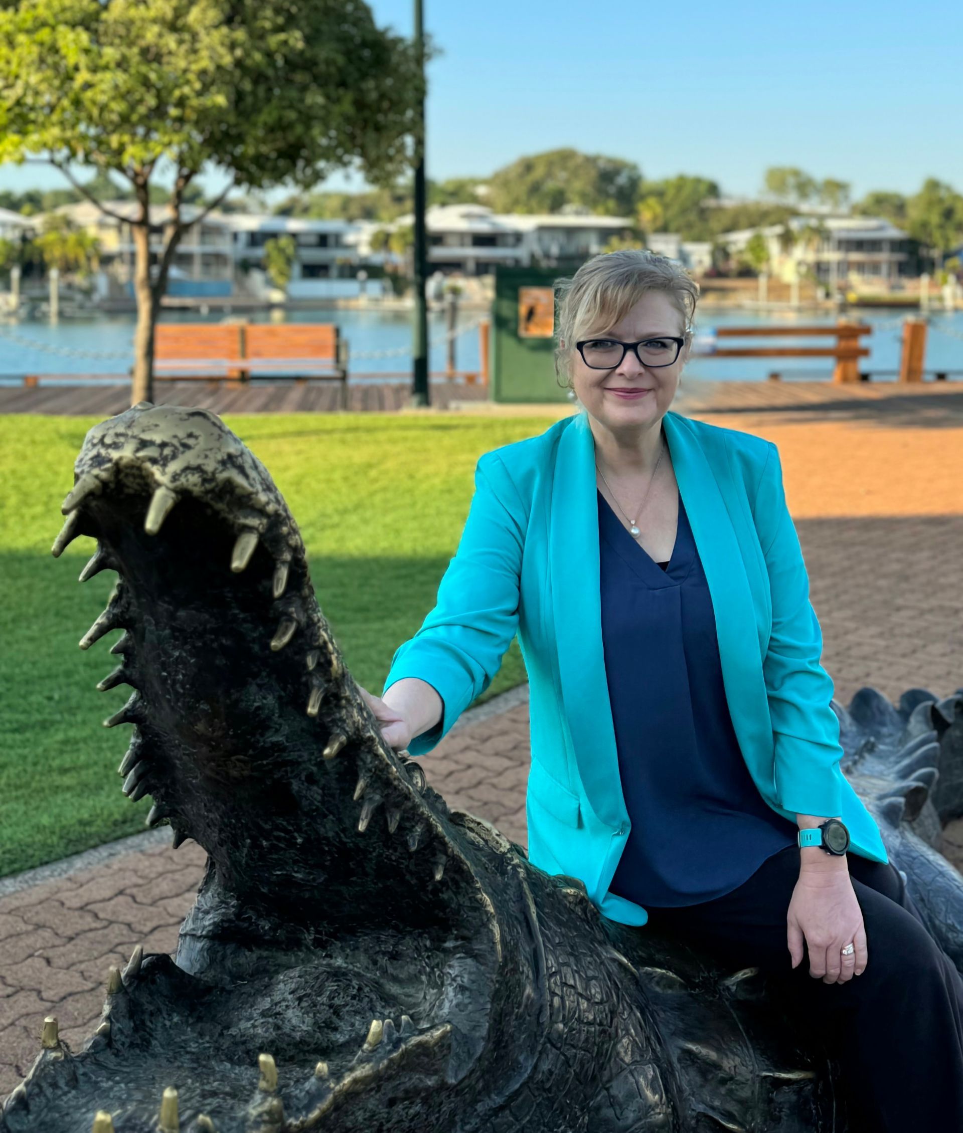 A woman in a blue jacket is sitting on a statue of a crocodile.
