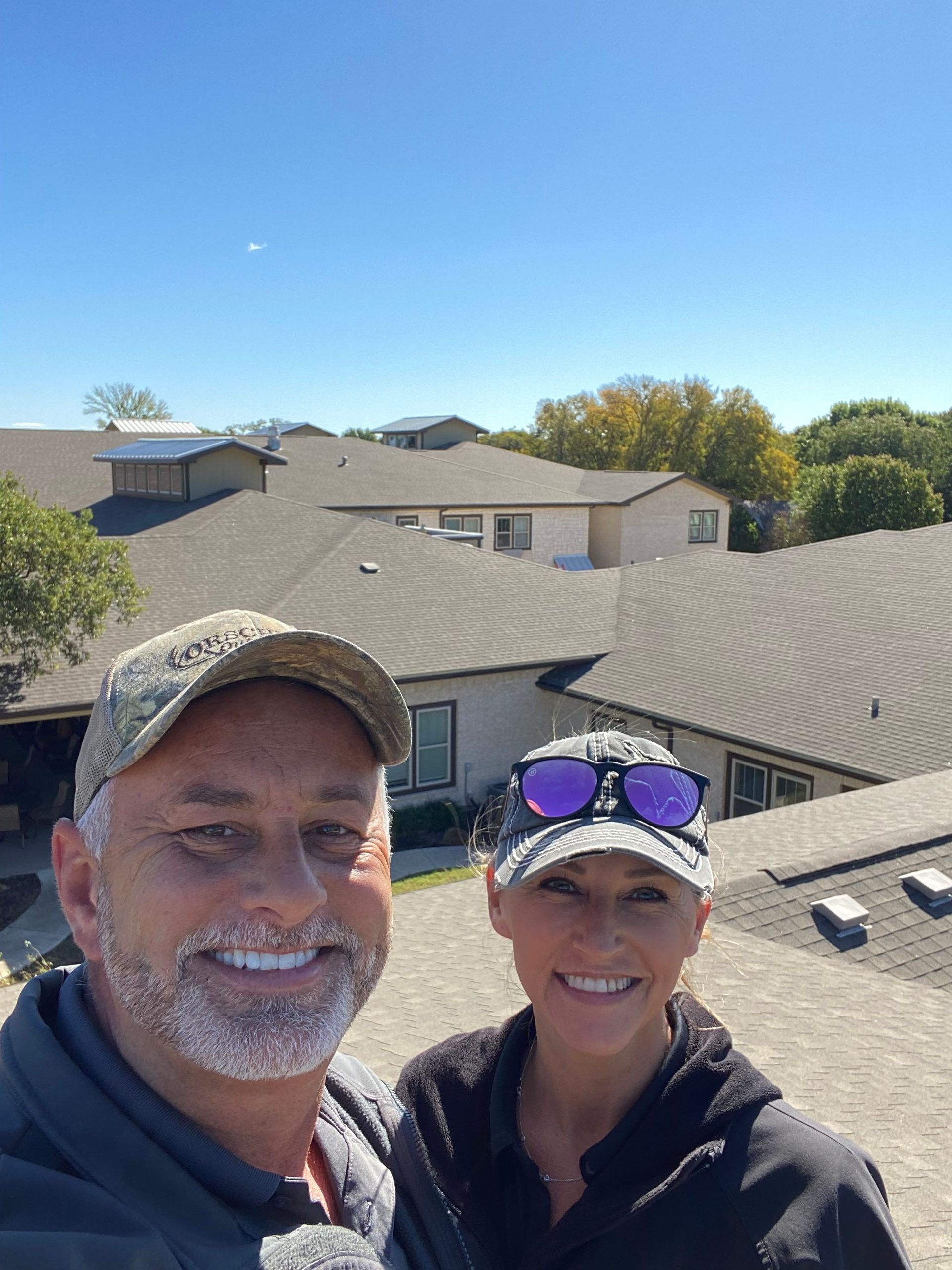Couple on a rooftop, smiling, with other houses in the background under a blue sky.