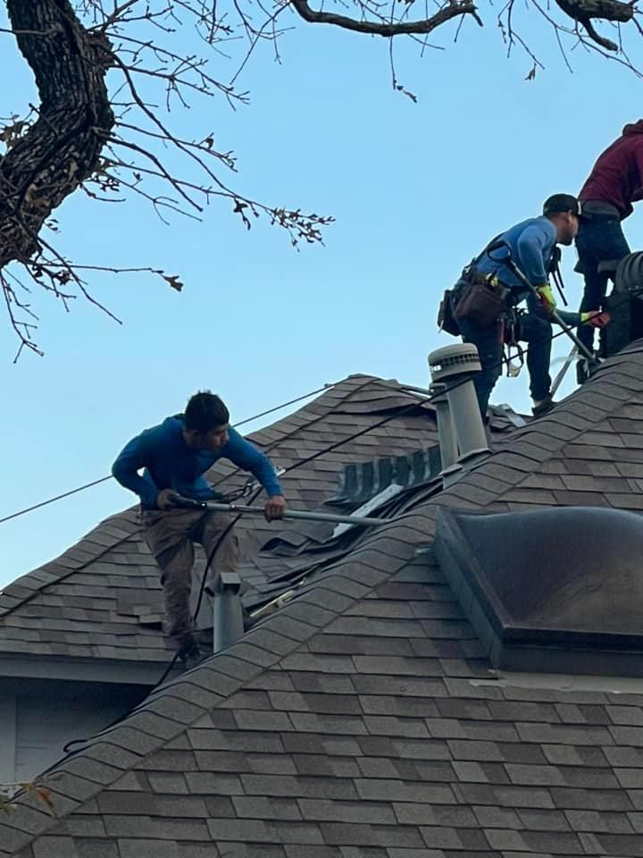Workers installing on a dark shingled roof under a bright blue sky. One man is holding a tool.