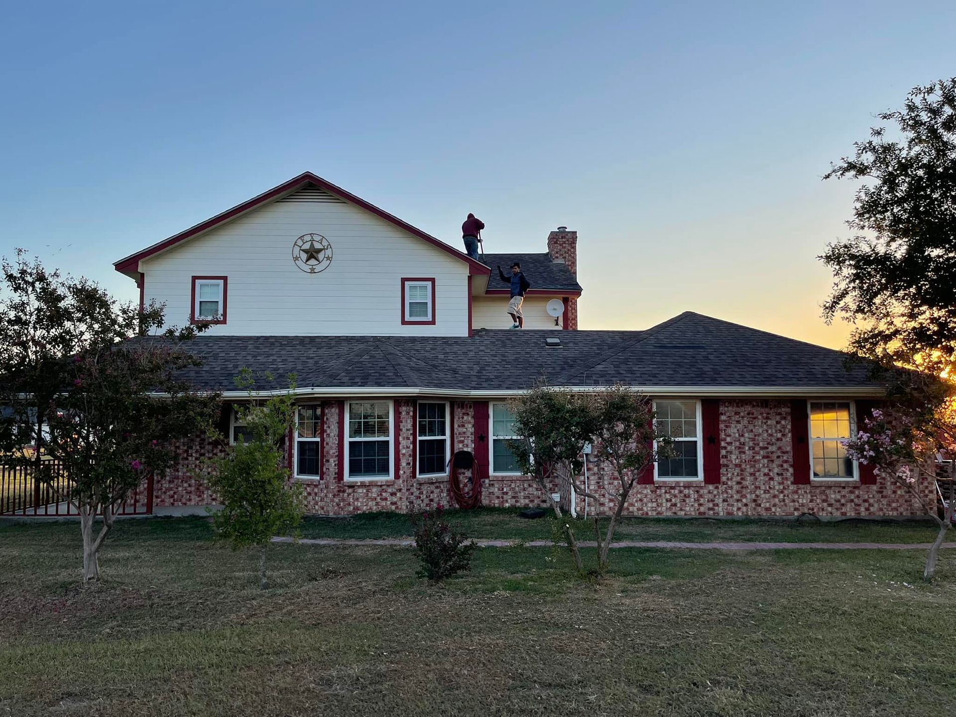 Two-story brick house with people on the roof during sunset.