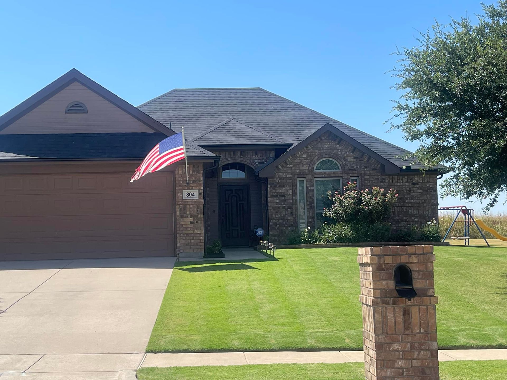 Brick house with green lawn, American flag, and mailbox.