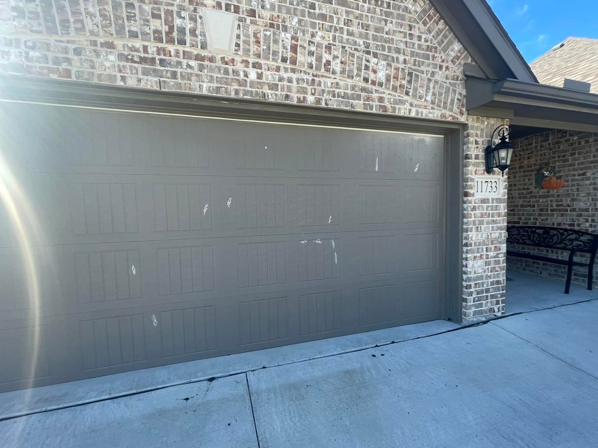 Gray garage door with white paint marks, brick house exterior, blue sky.