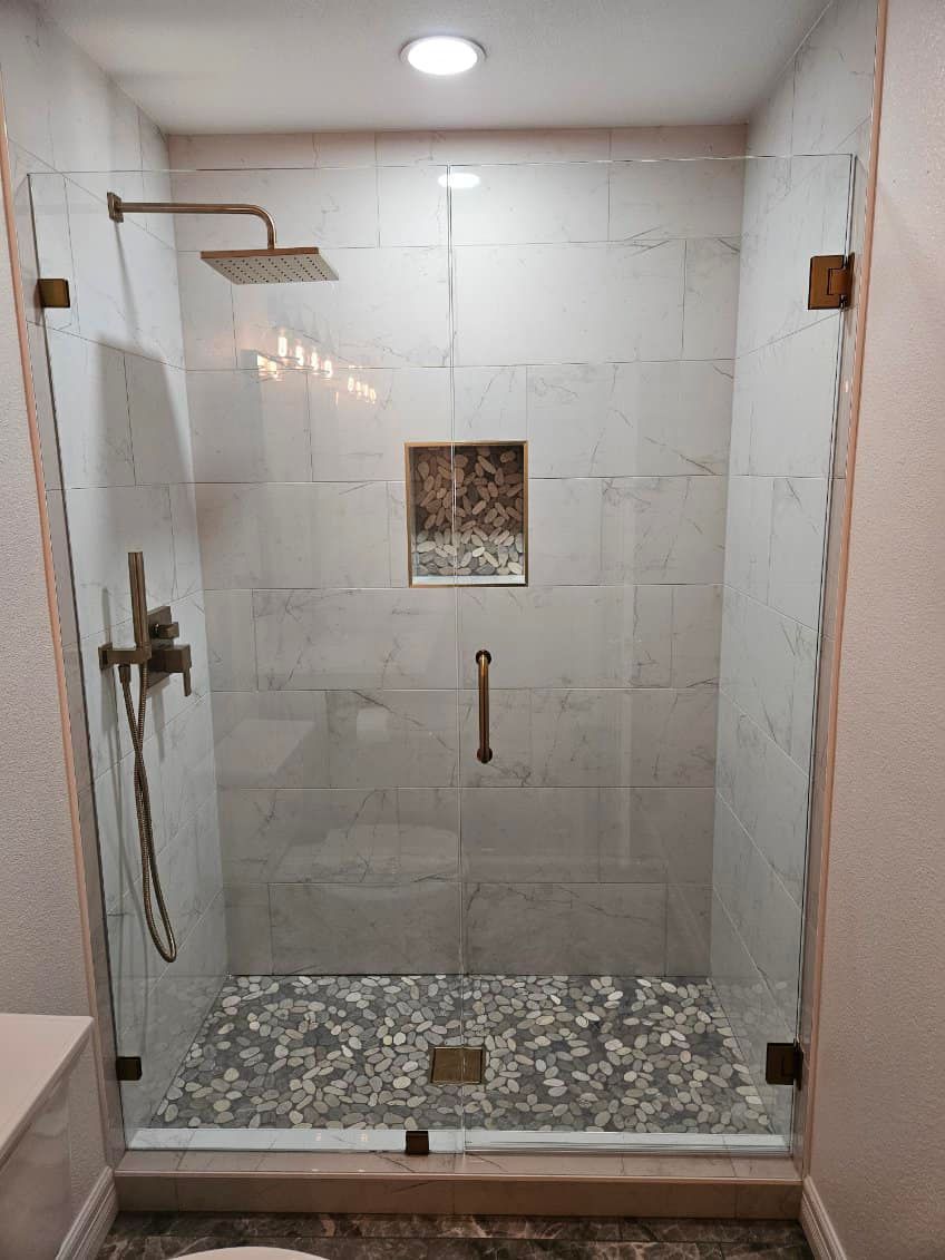 A modern, enclosed shower with glass doors, bronze hardware, and stone floor.