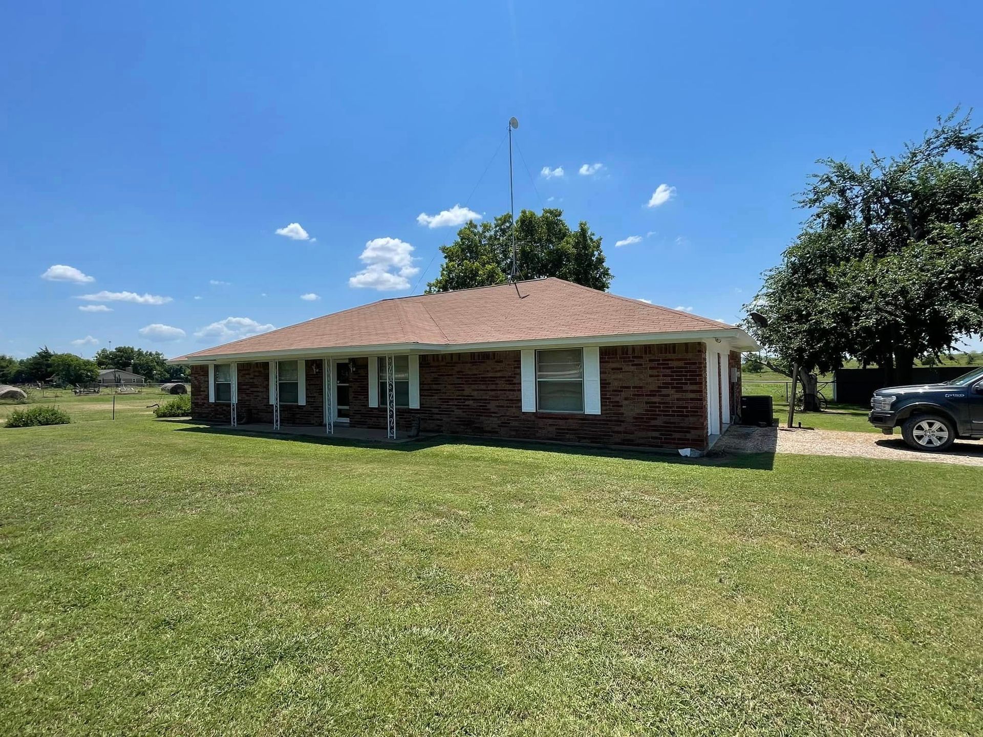 Brick ranch-style house on grassy lot under a blue sky; a car is parked near the driveway.