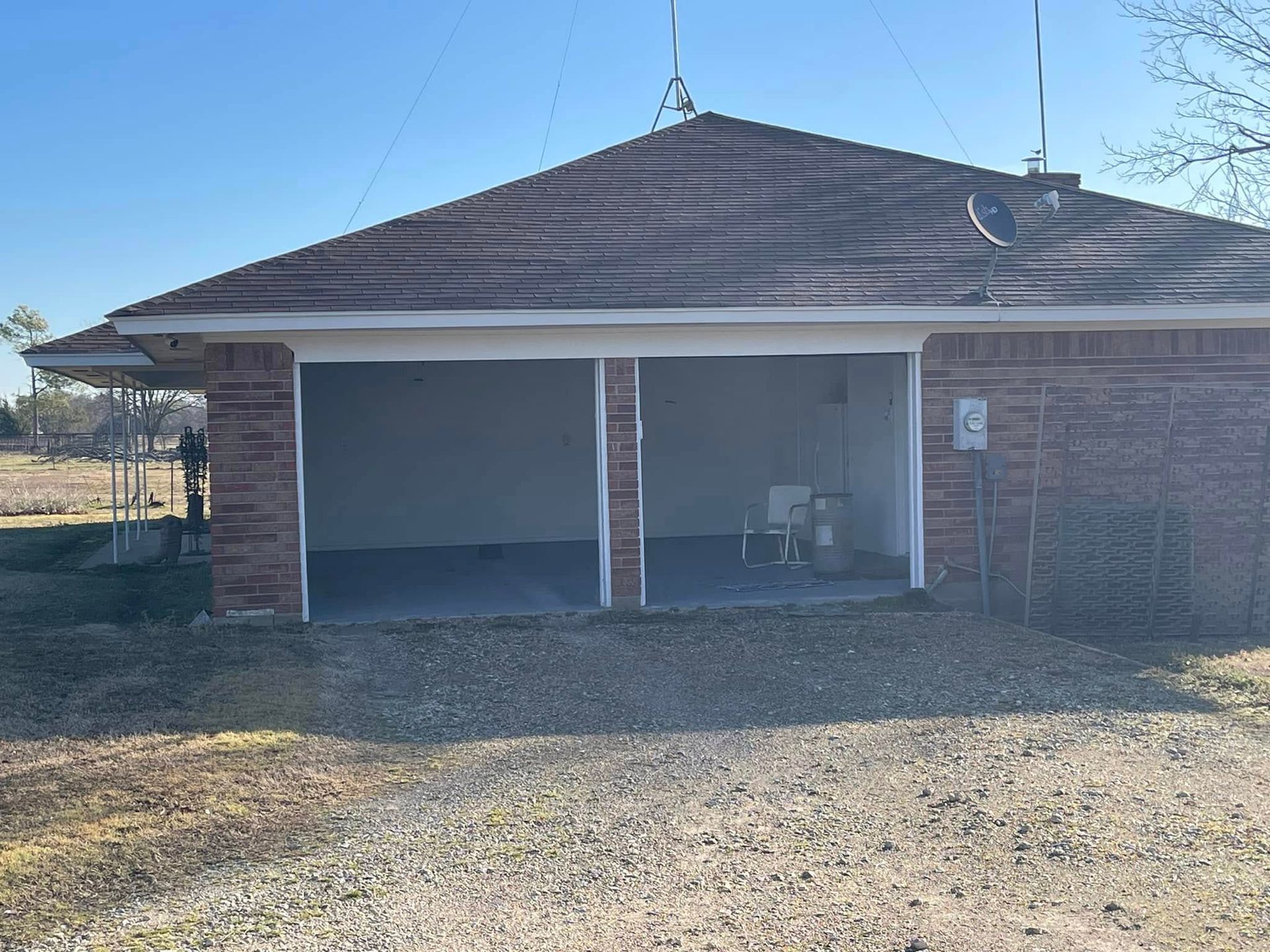 A two-car garage with open doors, brick exterior, and a brown roof, set against a clear blue sky.