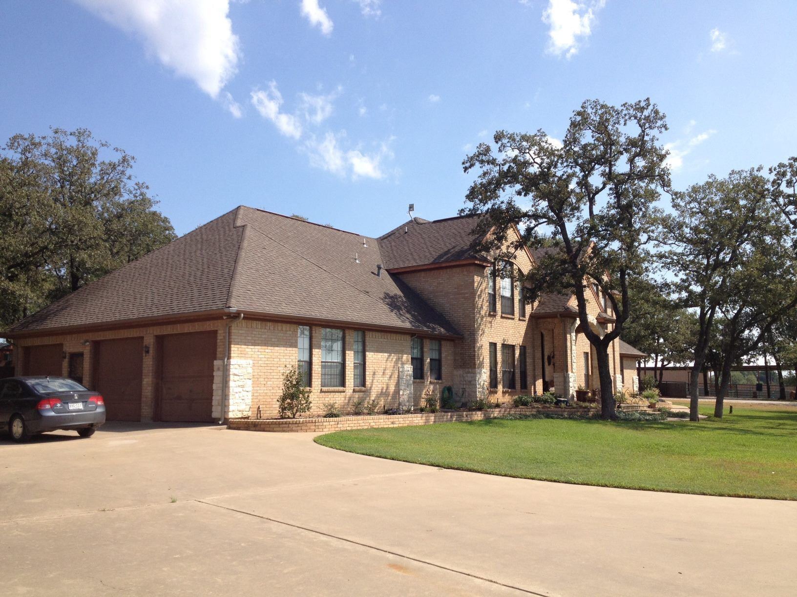 Beige brick house with brown roof, three-car garage, and circular driveway under a blue sky.