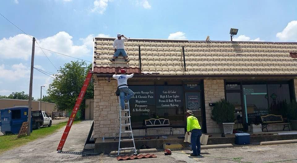 Three workers on a rooftop, one at the top of the ladder, repairing the roof of a building.