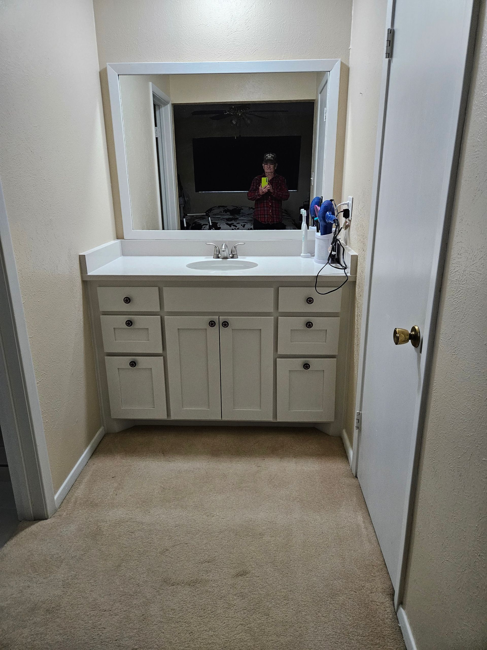 Bathroom with white vanity, mirror, and closed door on the right. Brown carpet and textured walls.