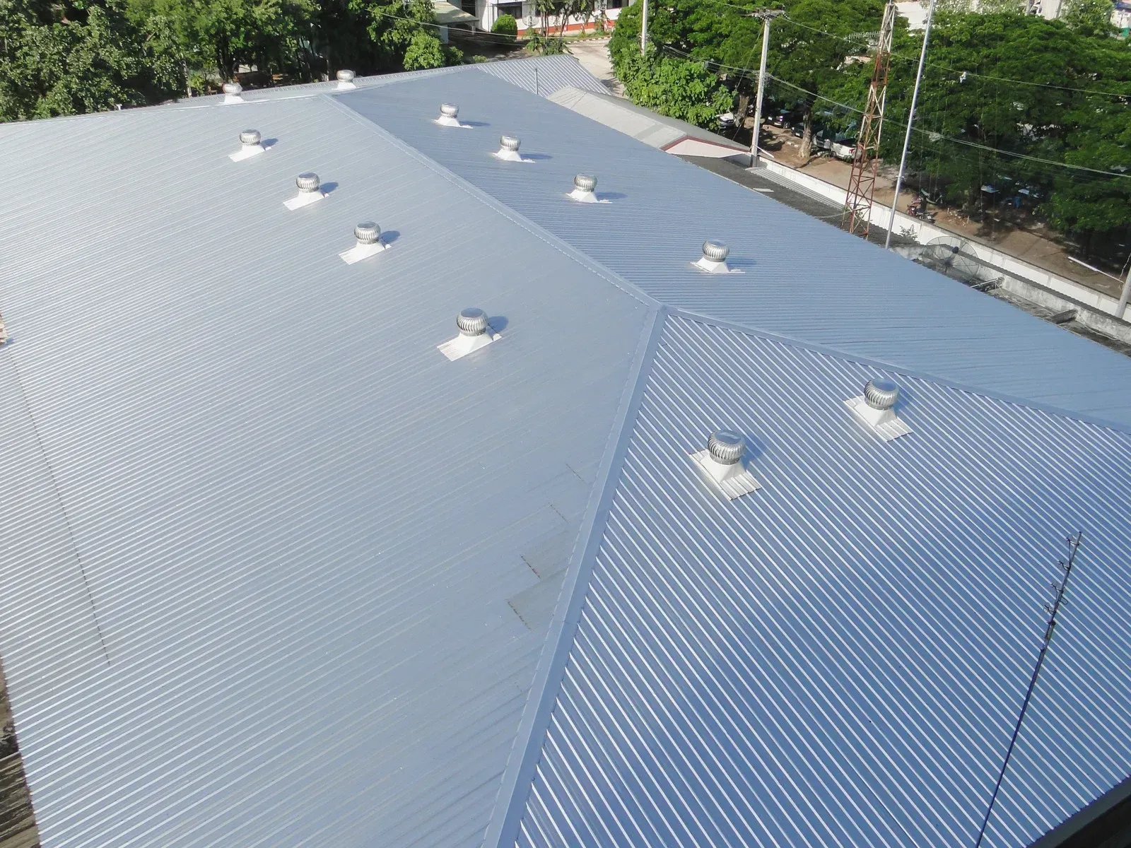 Roofers replacing a shingled roof on a brick building; red truck and trailer parked nearby.