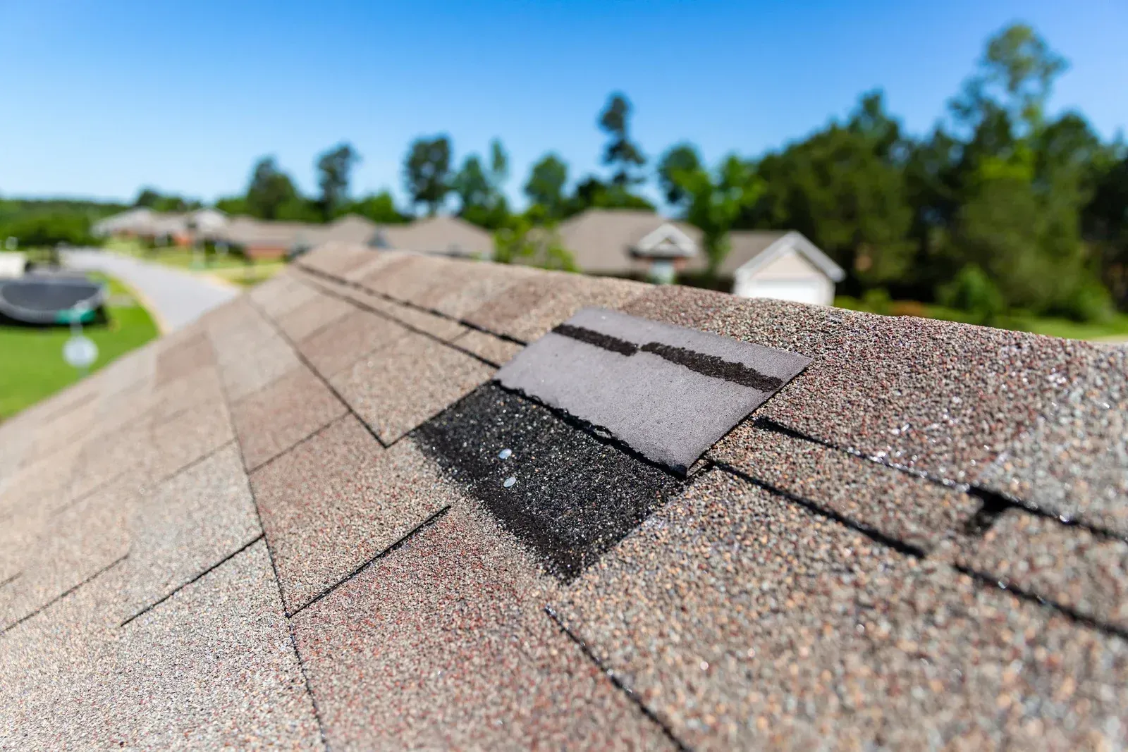 Roofer in red shirt repairing shingles with a hammer on a rooftop.