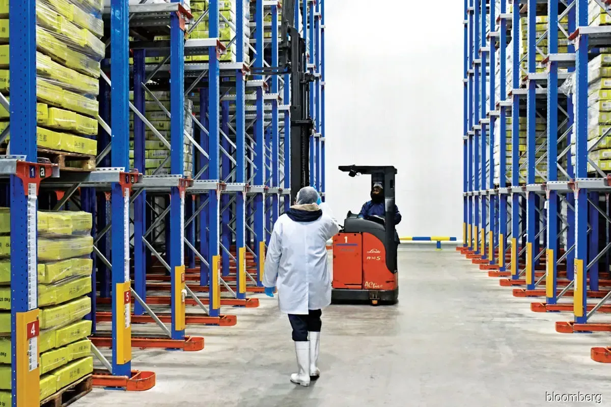 A man is walking in a warehouse next to a forklift.