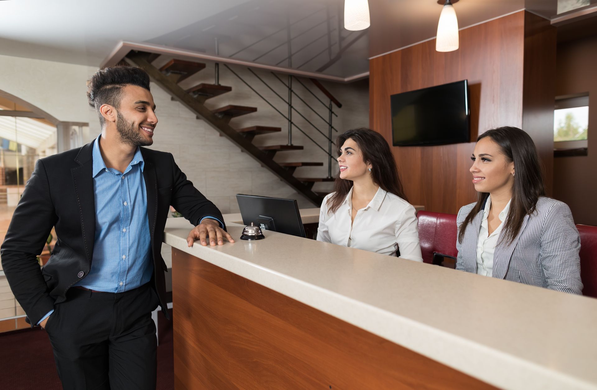 Businessman speaking with two receptionists at a hotel front desk in a modern lobby