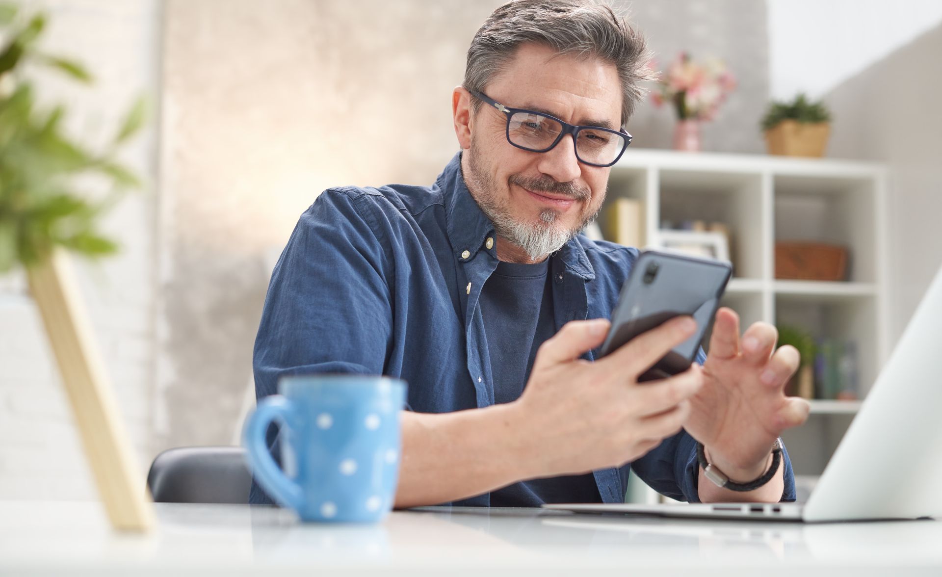 A man is sitting at a desk looking at his cell phone.