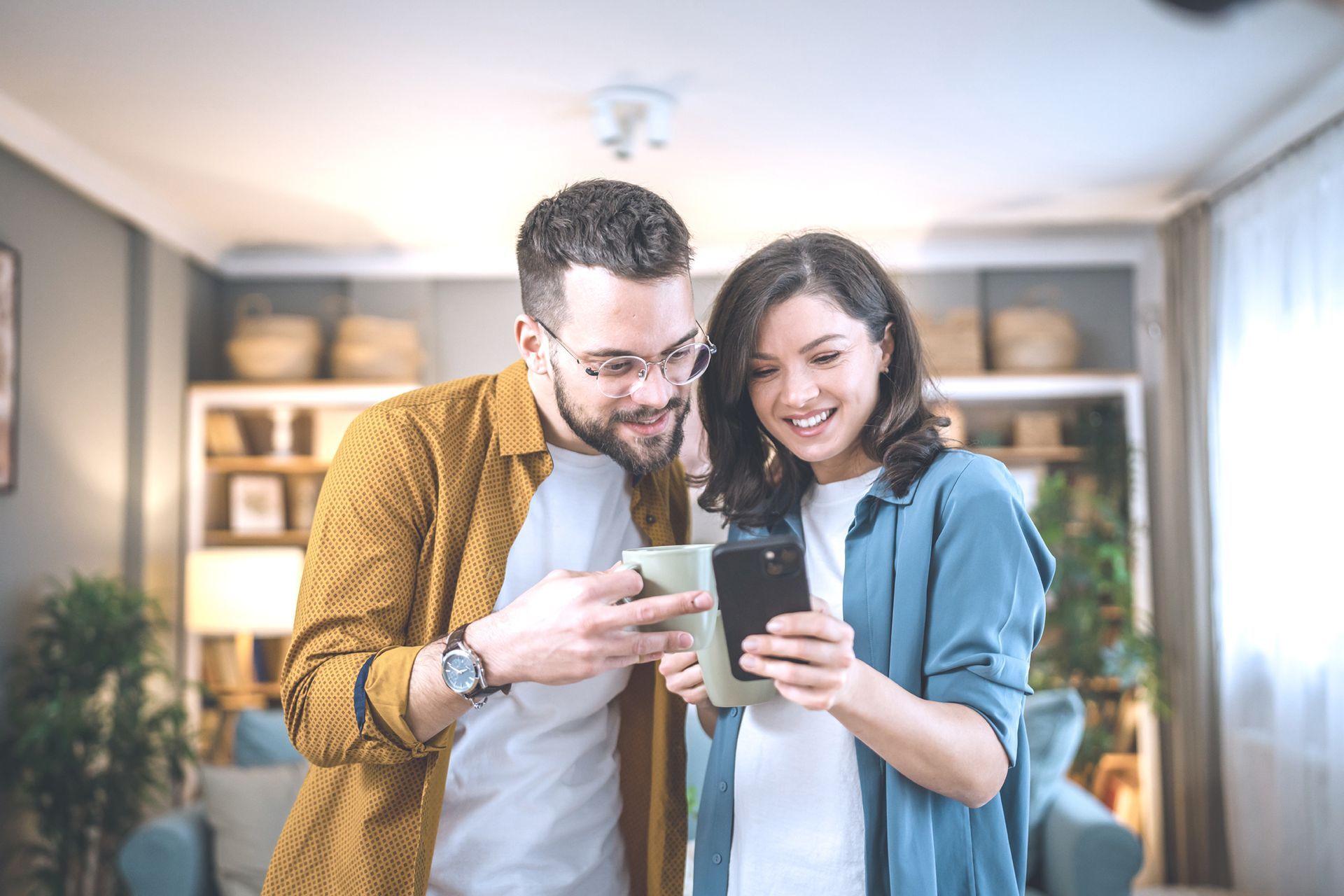 A man and a woman are looking at a cell phone together in a living room.