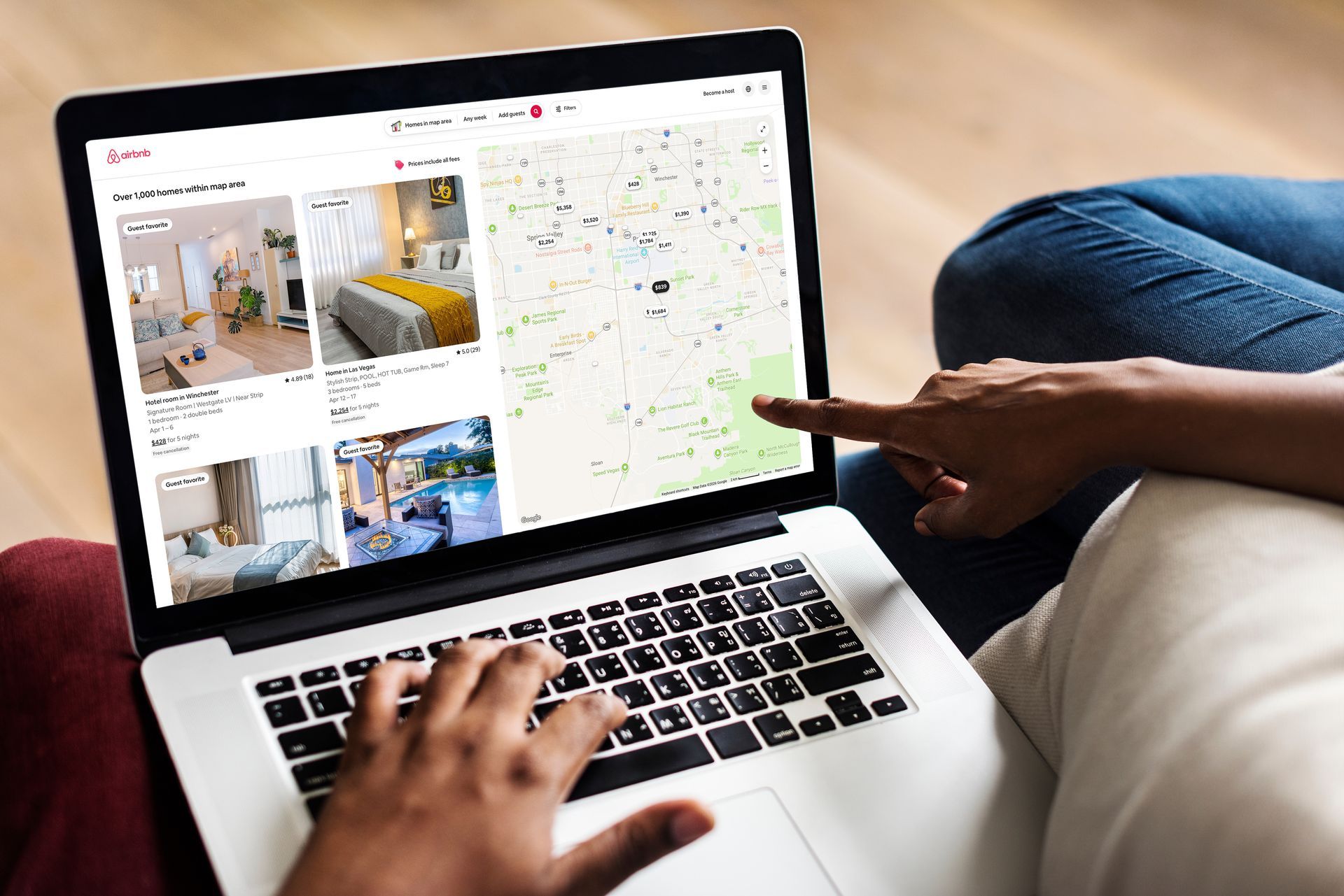 A person using a laptop to browse rental listings on an Airbnb-style website, with one hand typing and one pointing to a map.