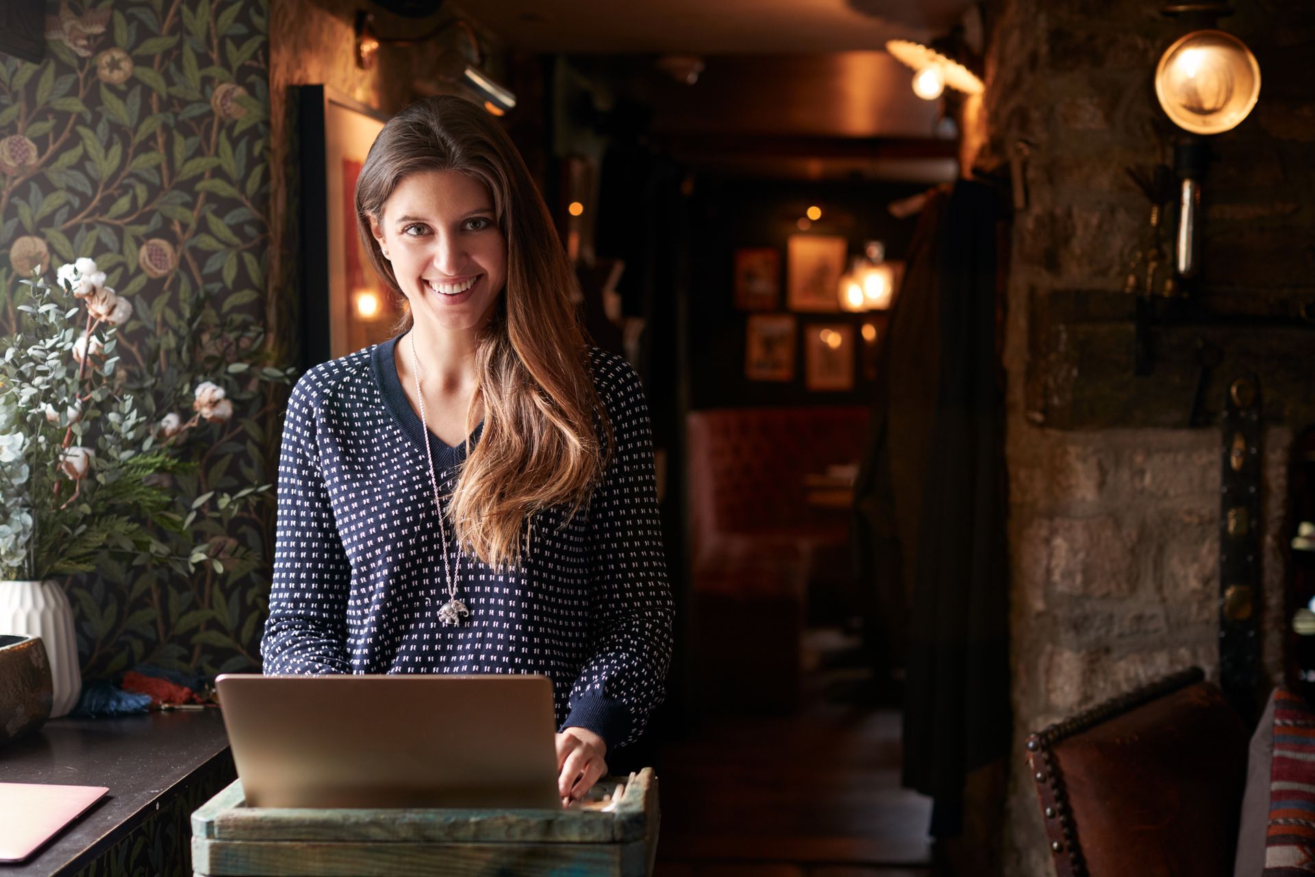 A woman is standing in front of a laptop computer in a restaurant.