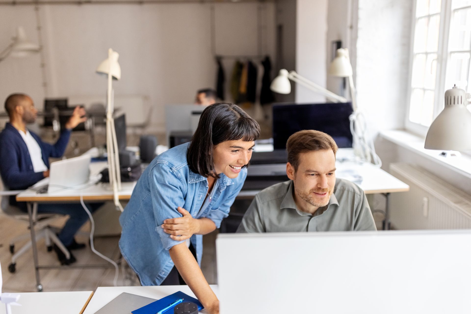 A man and a woman are looking at a computer screen in an office.