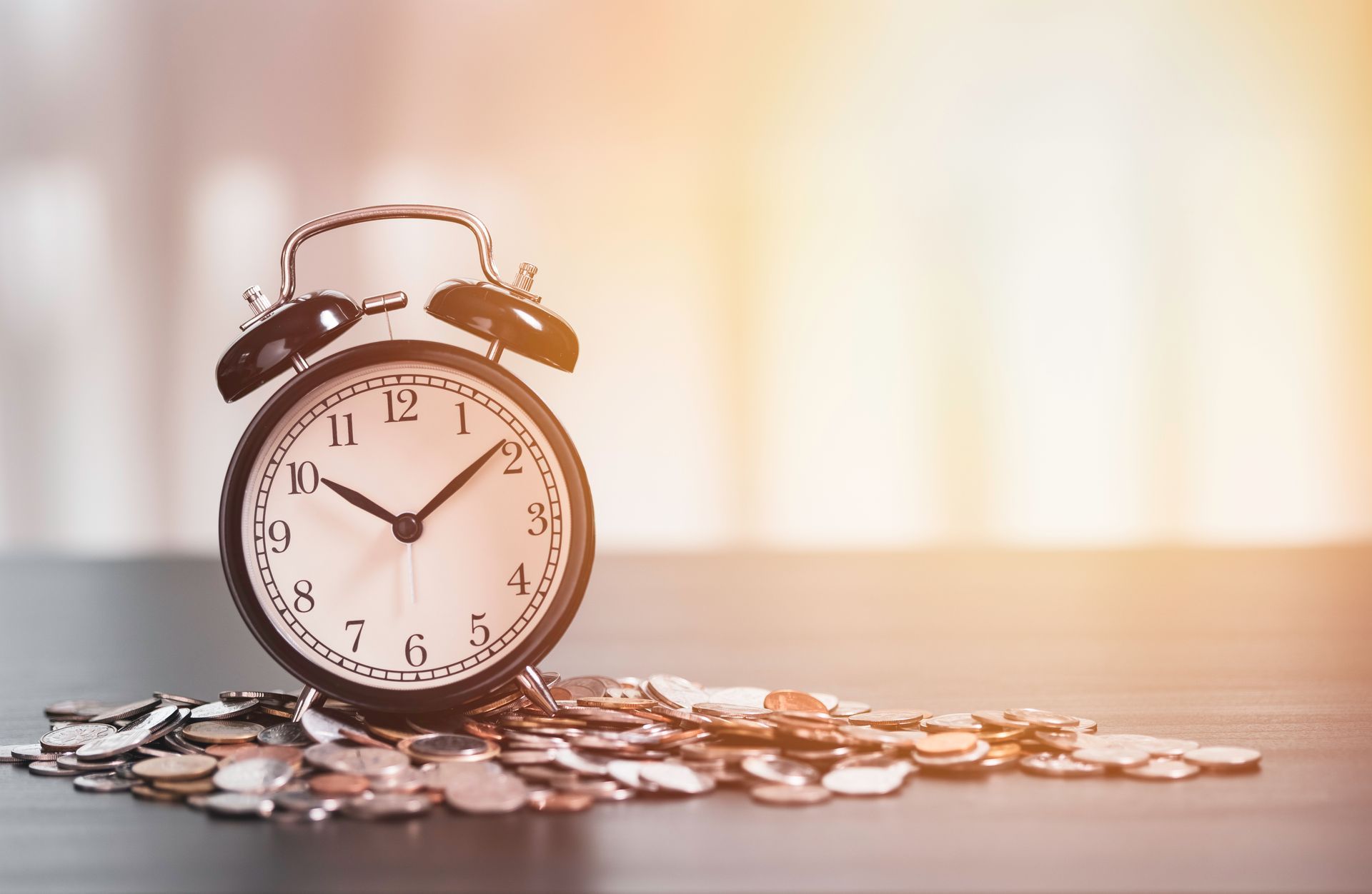 An alarm clock is sitting on top of a pile of coins on a table.