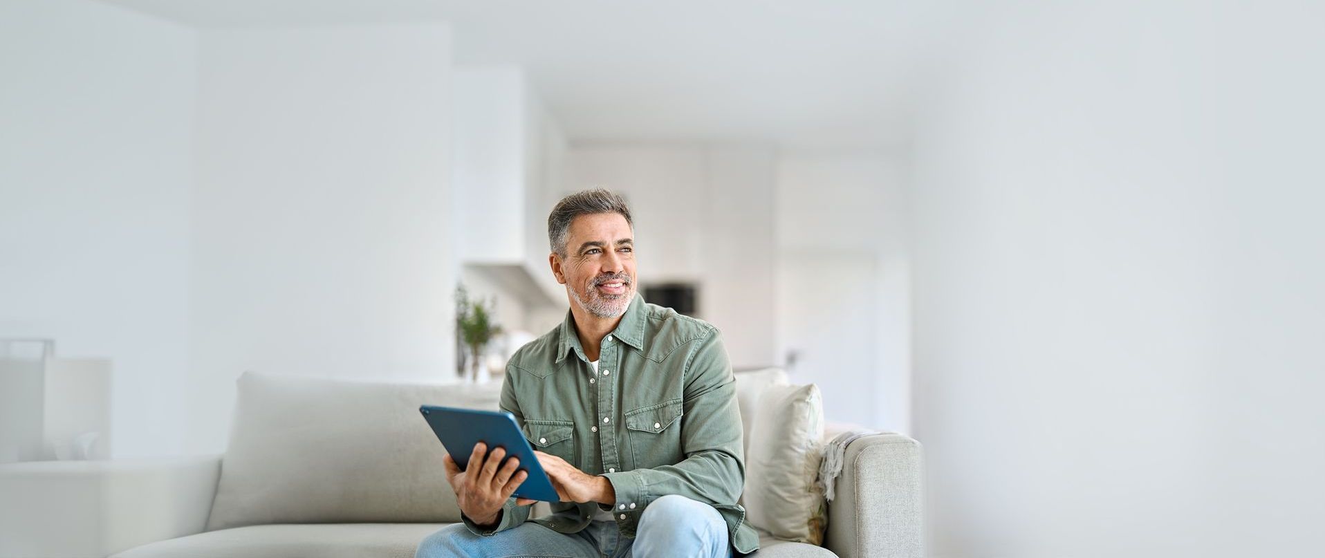 A man is sitting on a couch using a tablet computer.