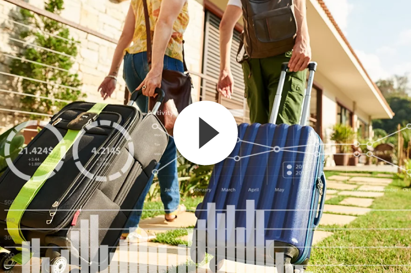 A man and a woman are walking with luggage in front of a house.