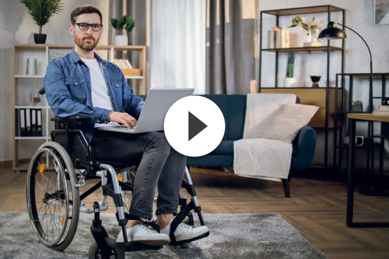 A man in a wheelchair is using a laptop computer in a living room.