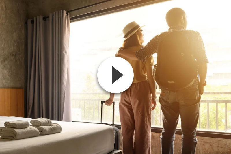 A man and a woman are standing in a hotel room looking out of a window.