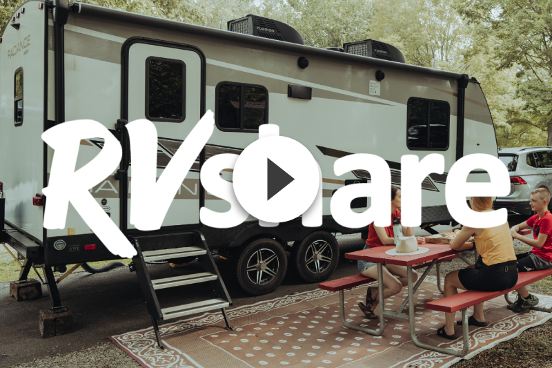 A group of people are sitting at picnic tables in front of a rv.