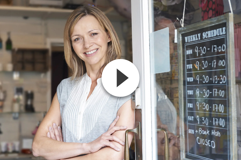 A woman is standing in front of a store door with her arms crossed.