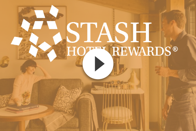 A man and woman are standing in a living room with the stash hotel rewards logo in the background