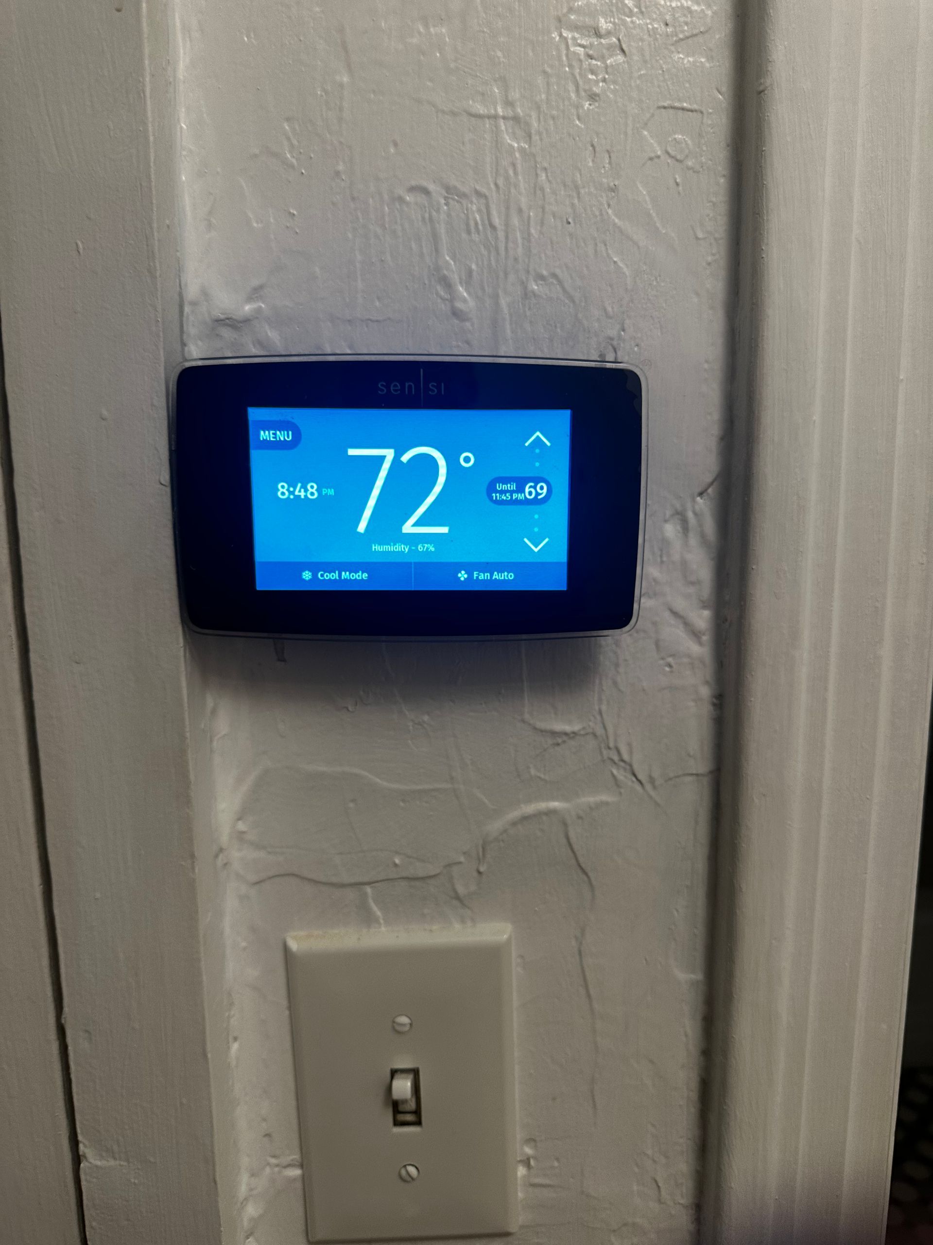 A thermostat is hanging on a wall and the temperature is 72 degrees.