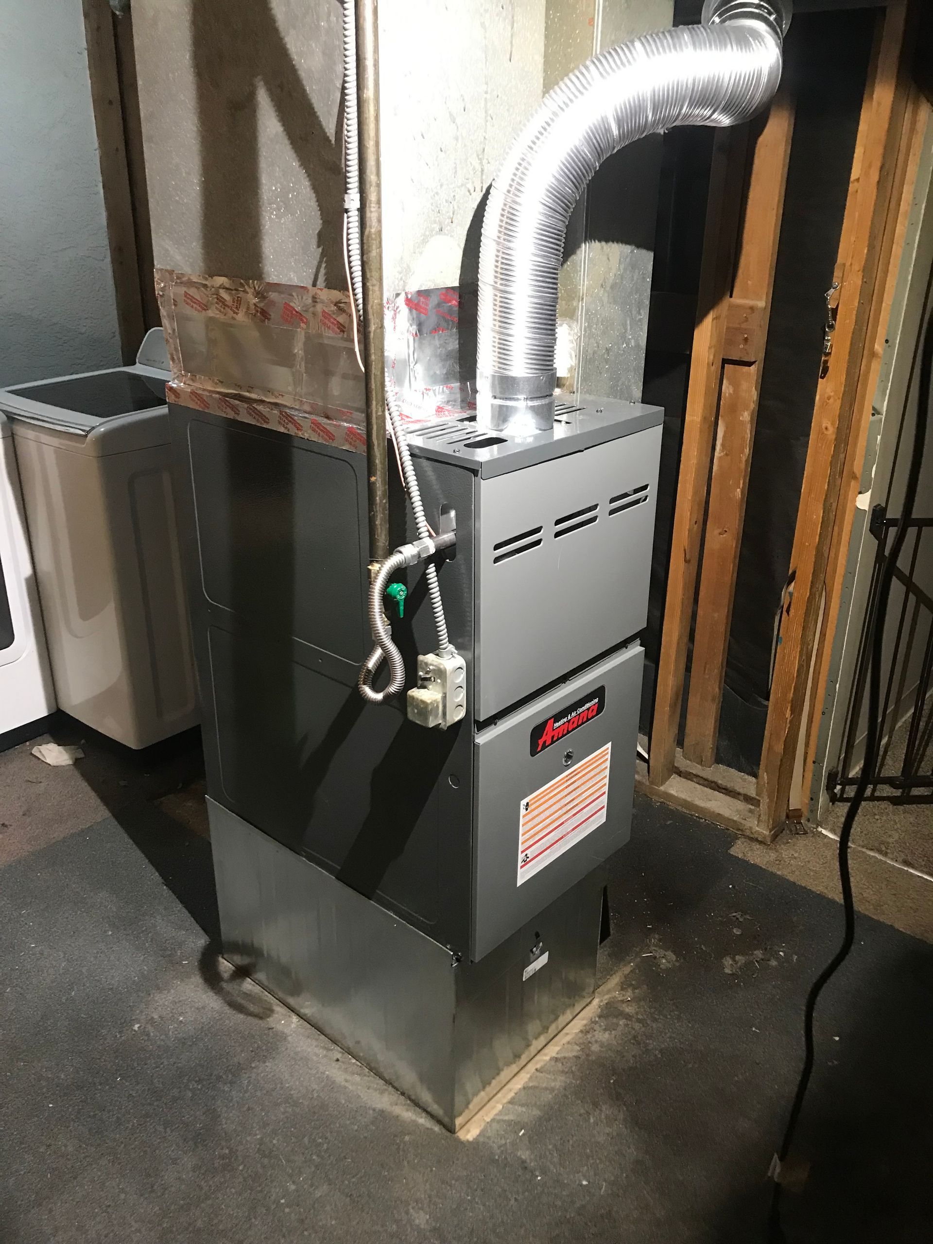 A furnace is sitting in a basement next to a wall.