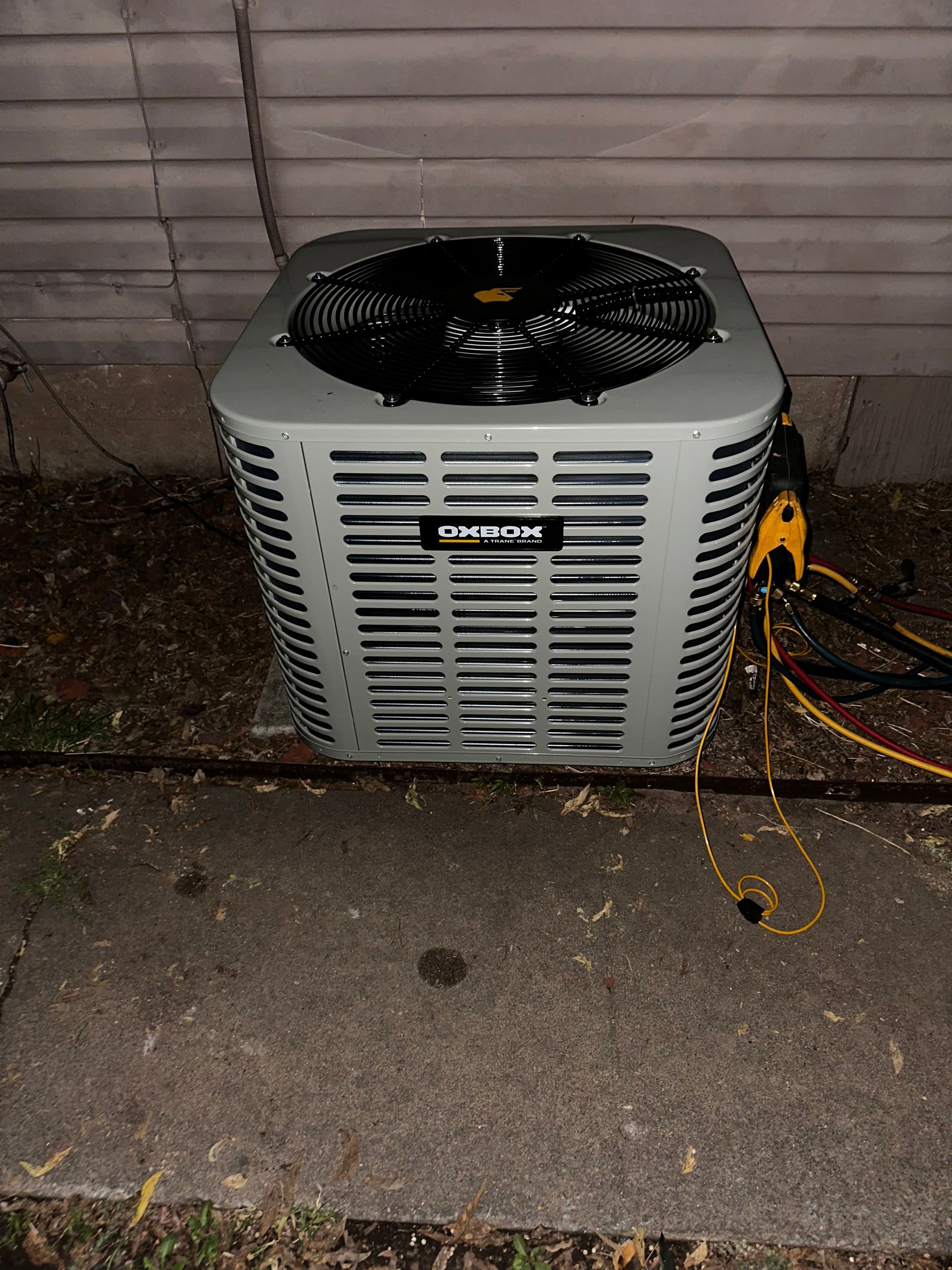 An air conditioner is sitting on the sidewalk next to a house.