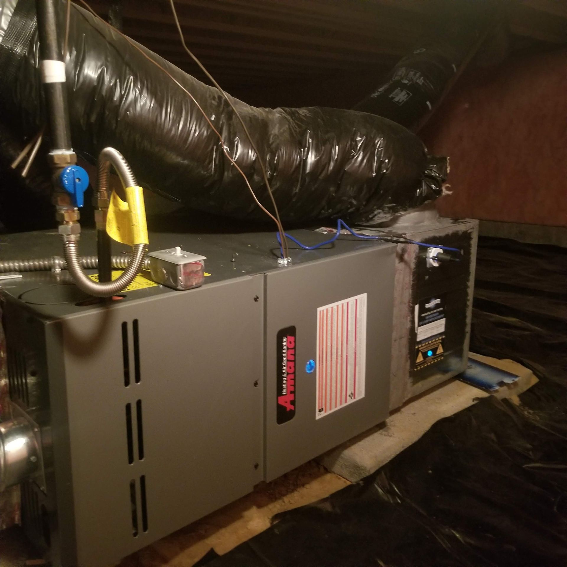 An air conditioner is sitting in the attic with a hose attached to it.
