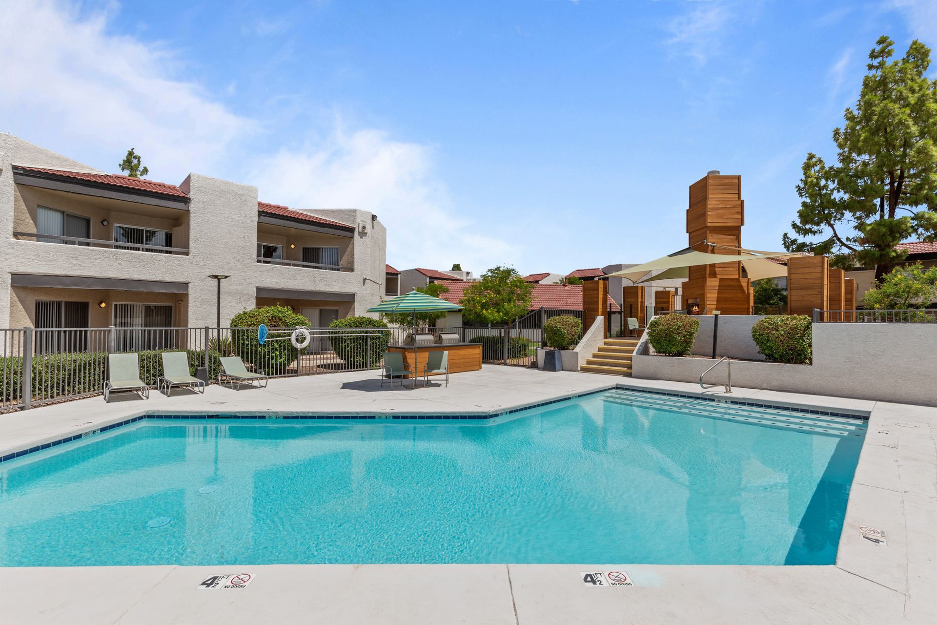 A large swimming pool is surrounded by chairs and umbrellas in front of a building at Citrine on 67th.