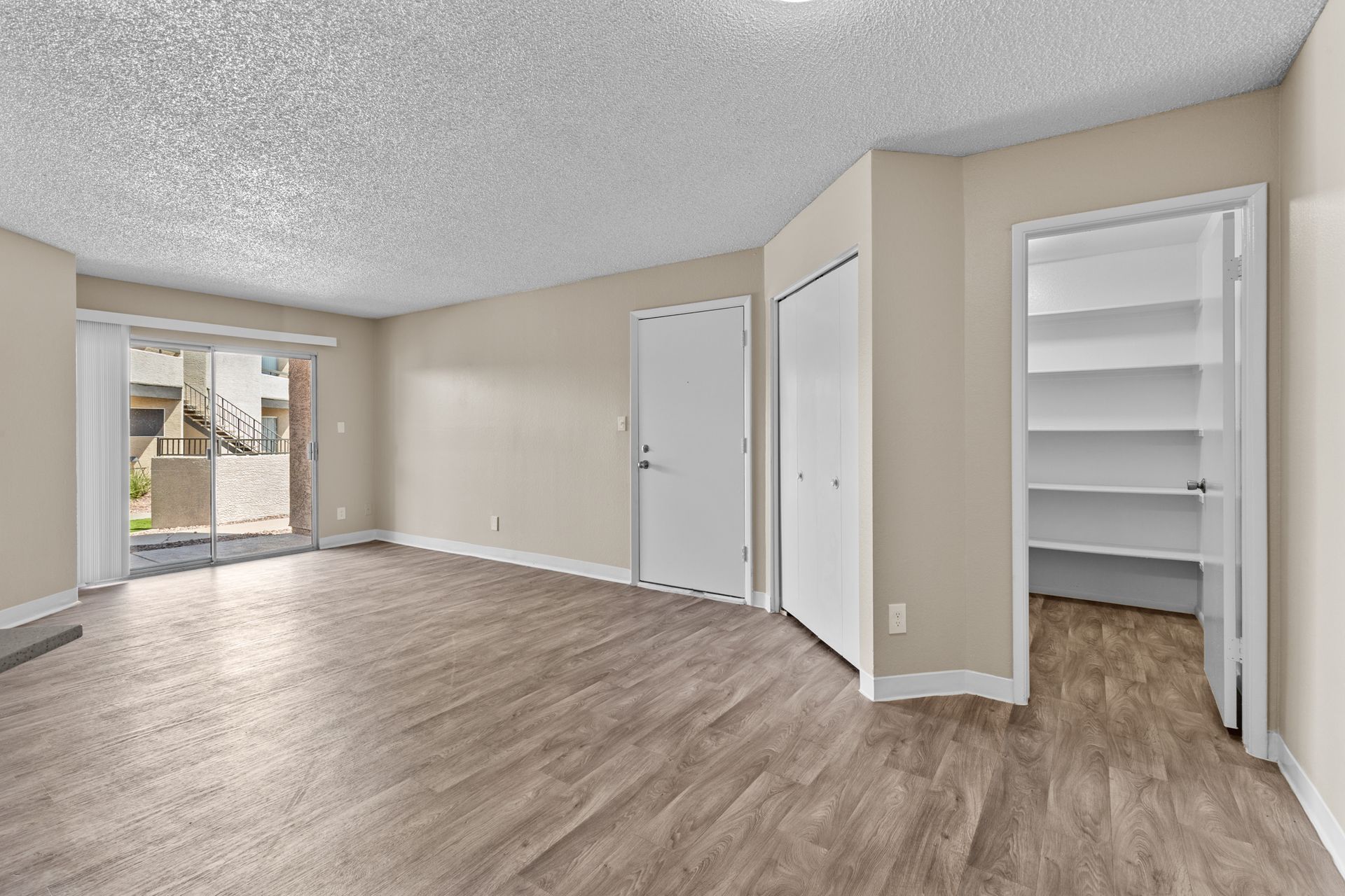 An empty living room with hardwood floors and a sliding glass door at Citrine on 67th.