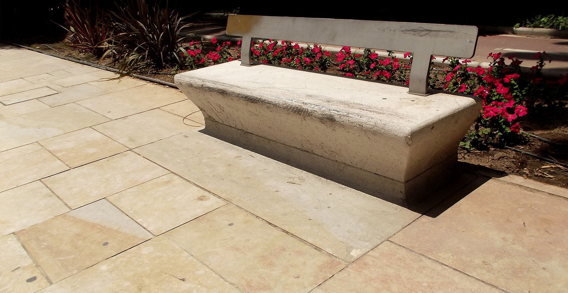 A concrete bench is sitting on a sidewalk in a park