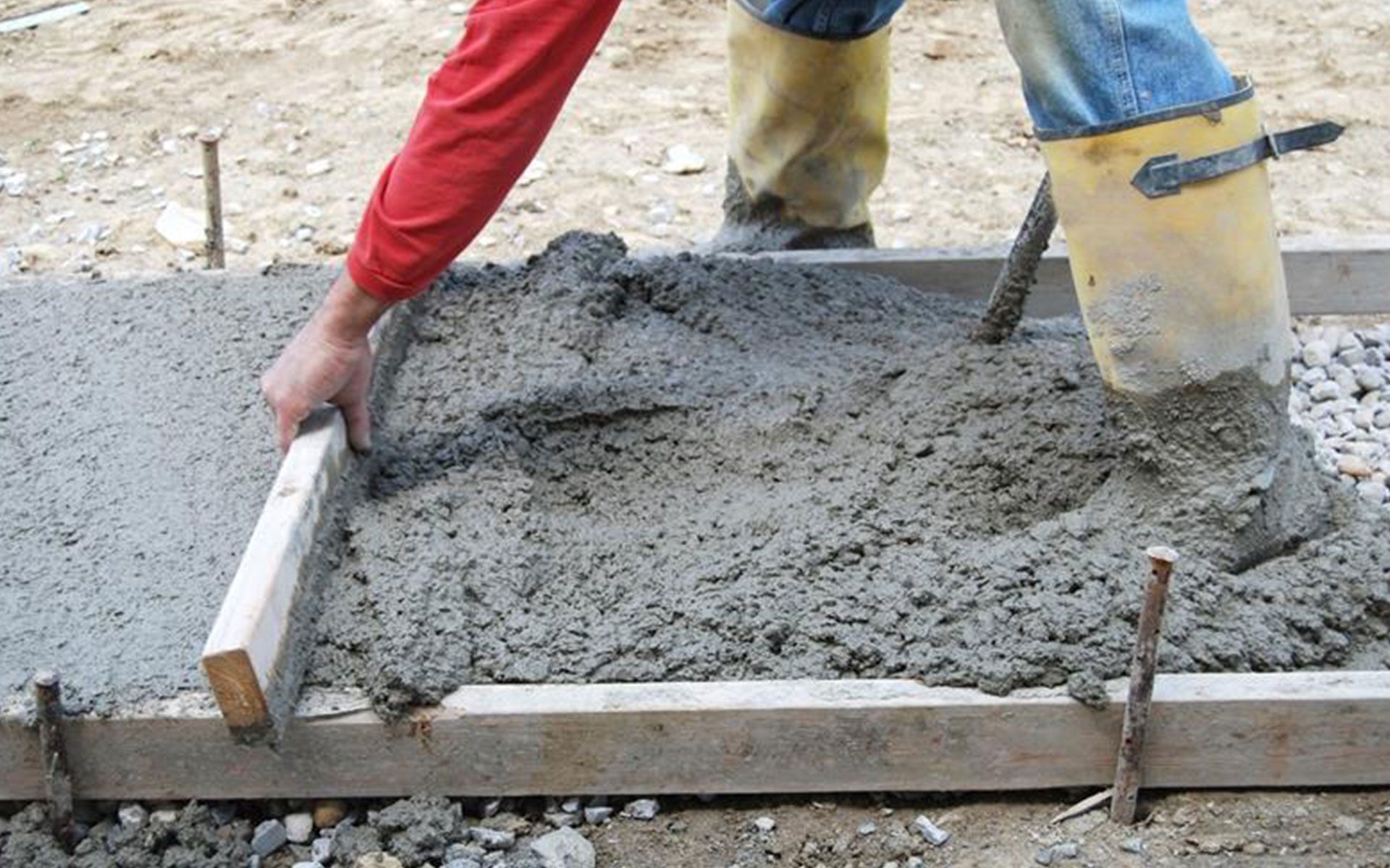 A person is pouring concrete into a wooden frame