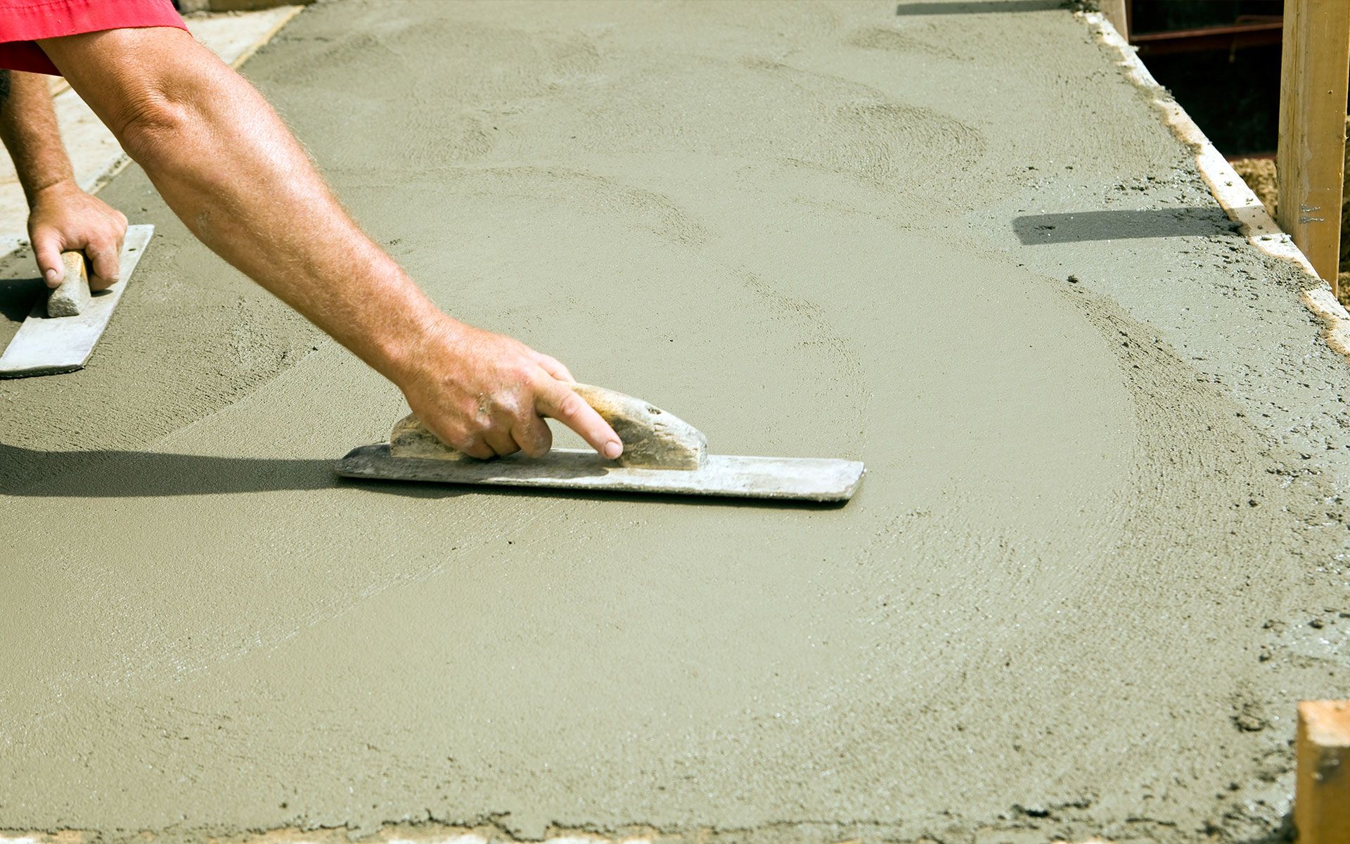 A man is using a trowel to spread concrete on a sidewalk.
