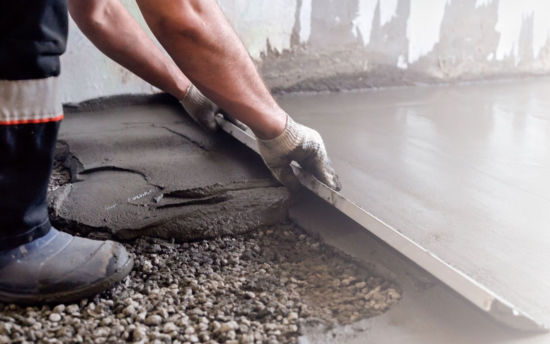 A man is laying concrete on the floor with a trowel.